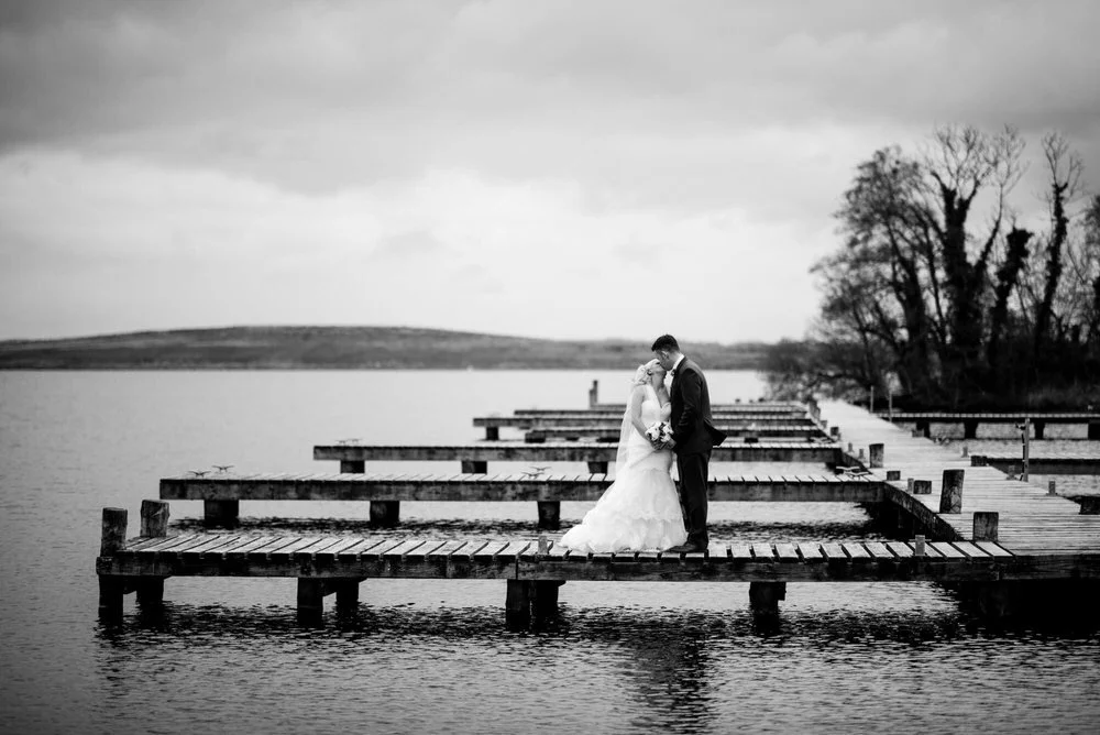 Bride and groom embracing on a wooden jetty on Lough Erne at Lusty Beg Island, in black and white
