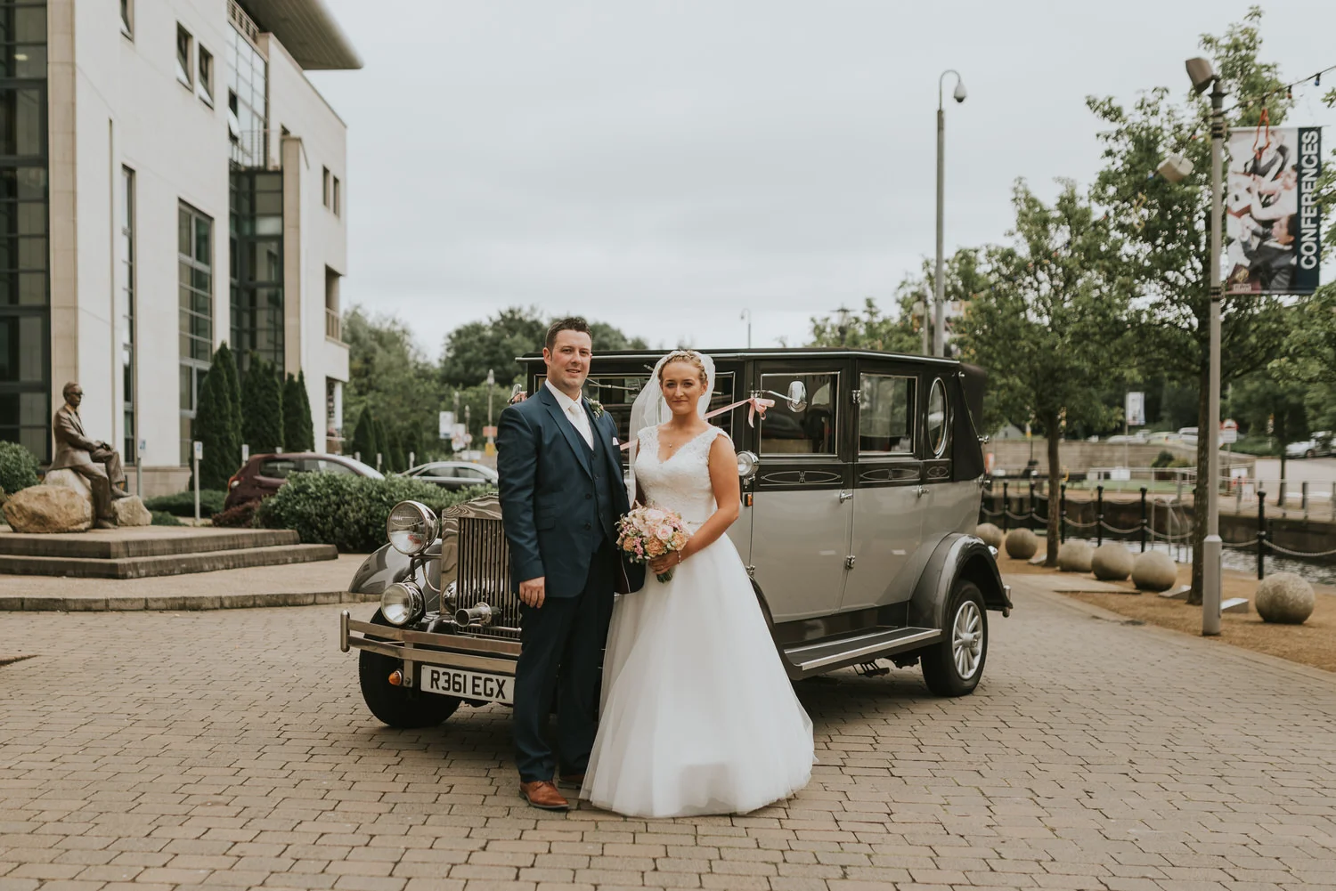 Bride and groom standing beside a vintage wedding car outside Lagan Valley Island, Lisburn