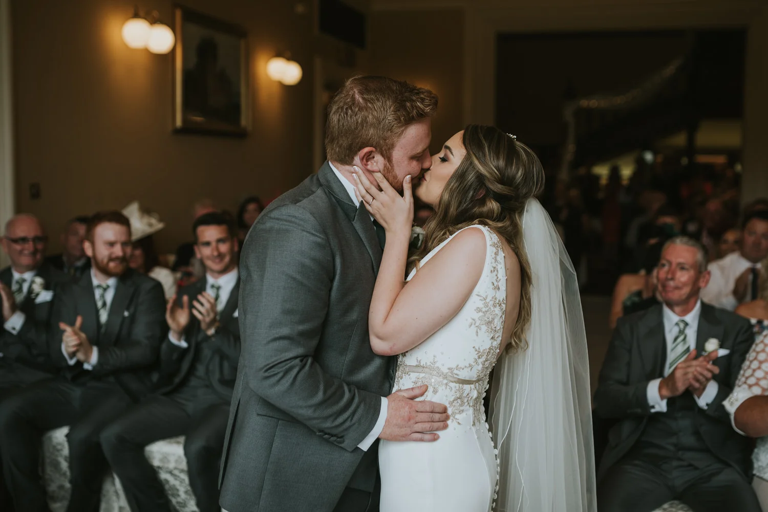 Bride and groom kissing at the end of their ceremony at Belfast Castle while their guests applaud