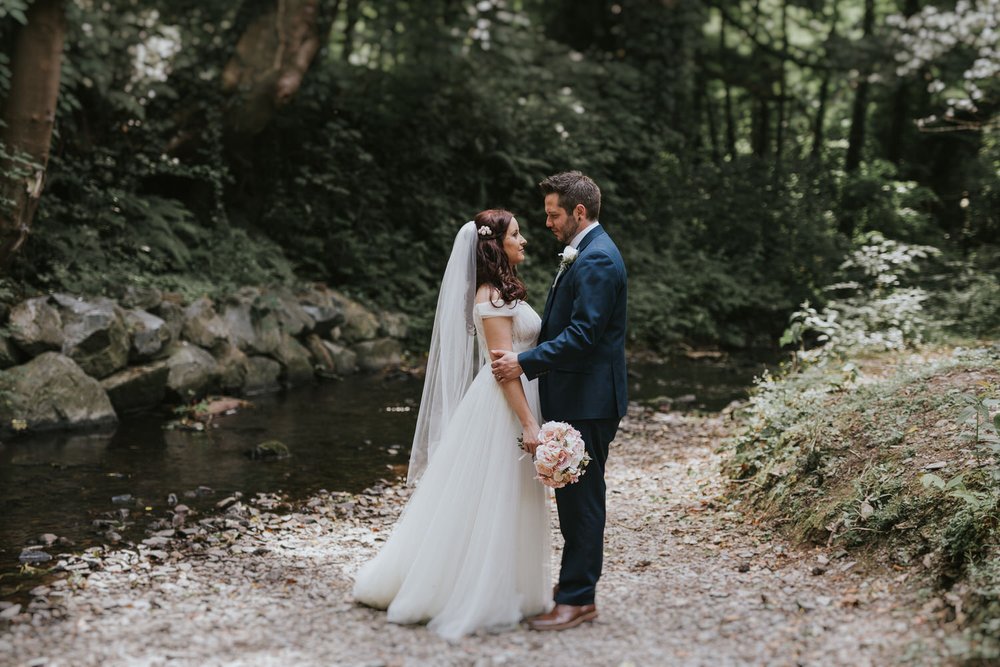 Katrina and Jason standing beside a stream in the woodland at Clandeboye Lodge