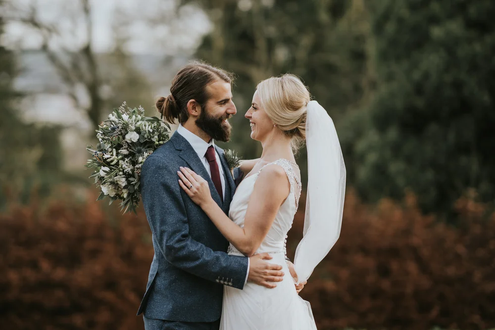 Aisling and Antony smiling at each other in an embrace in the gardens at Belfast Castle