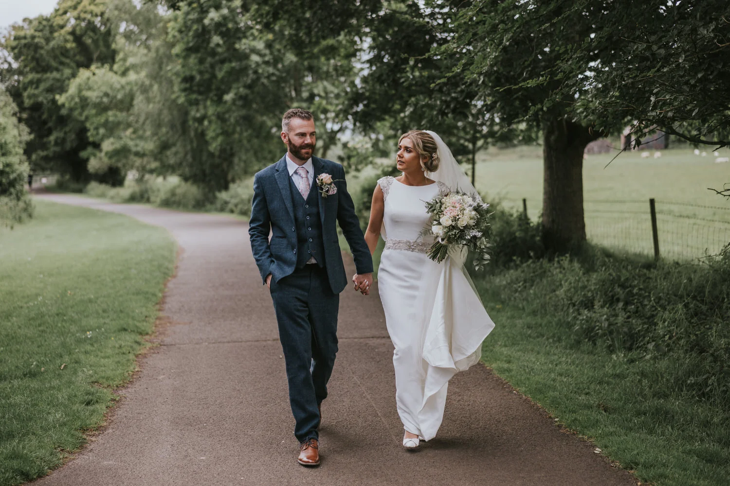 Bride and groom walking along a path beside parkland at Roe Valley Resort