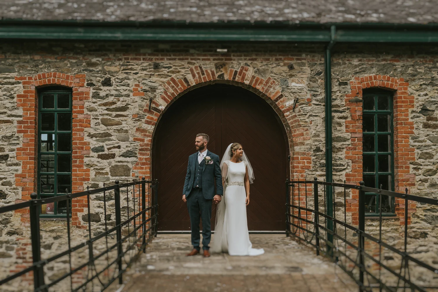 Bride and groom standing in front of an old stone building with an arched wooden door at Roe Valley Resort