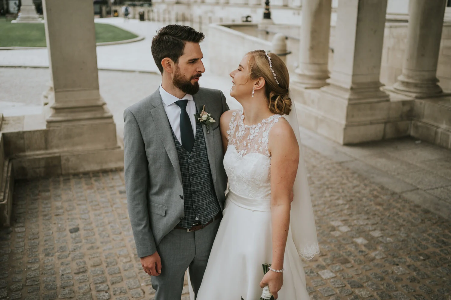 Bride and groom looking at each other between stone columns at Belfast City Hall