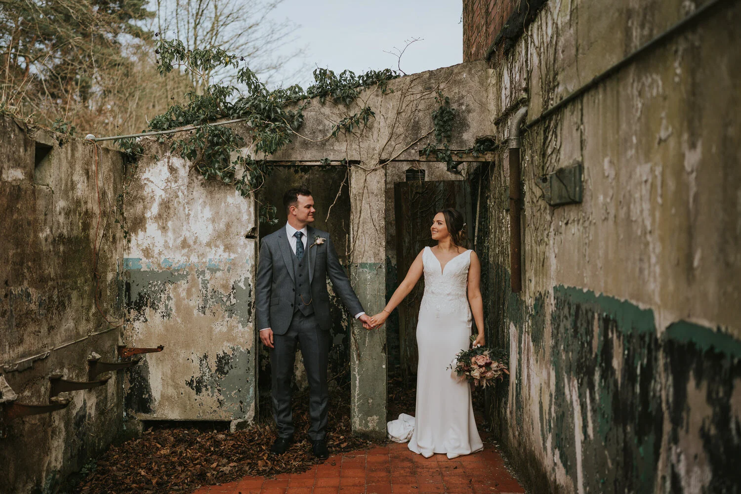 Bride and groom holding hands in an old stone courtyard with ivy at The Wool Tower