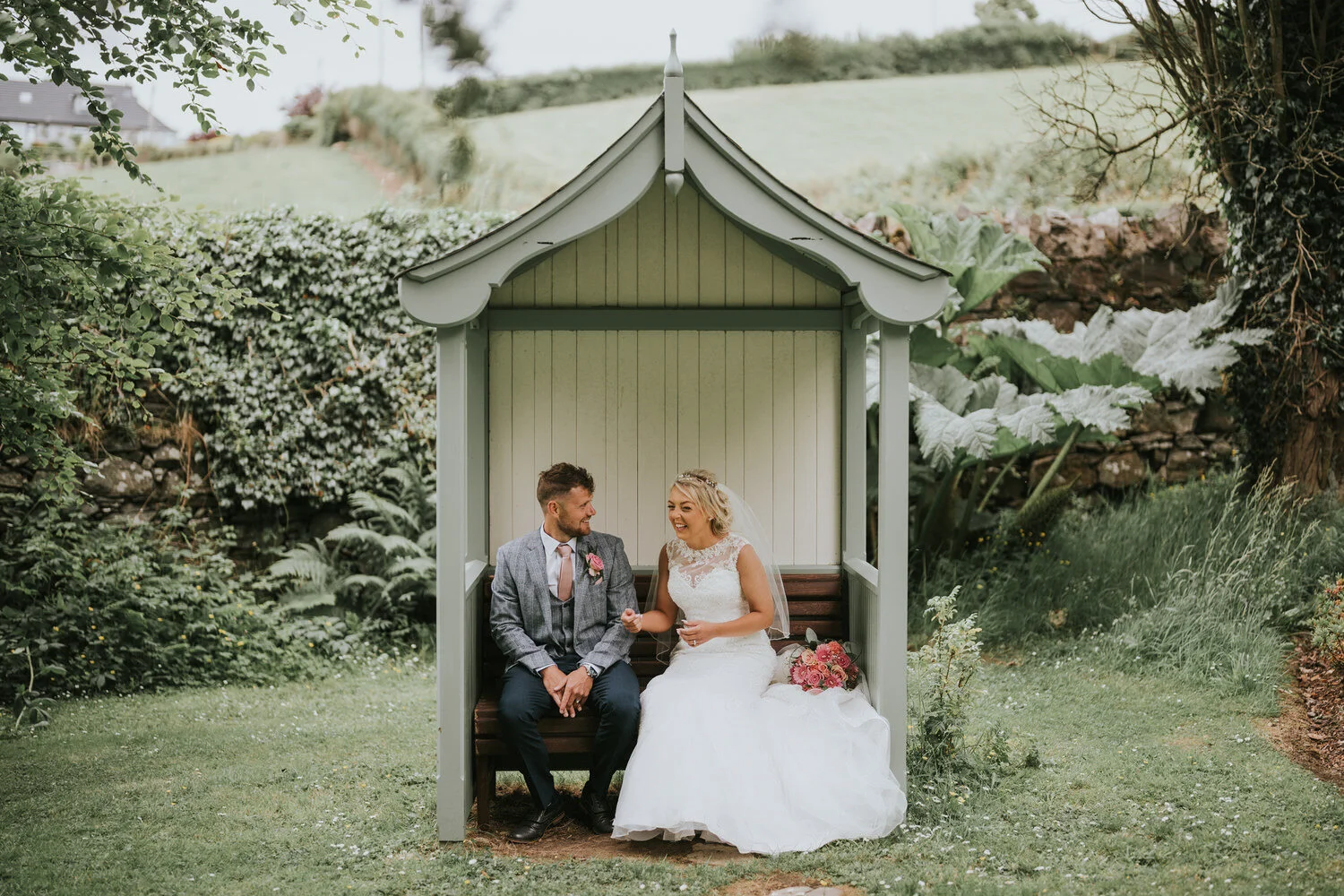 Bride and groom sitting together in a garden arbour at Millbrook Lodge