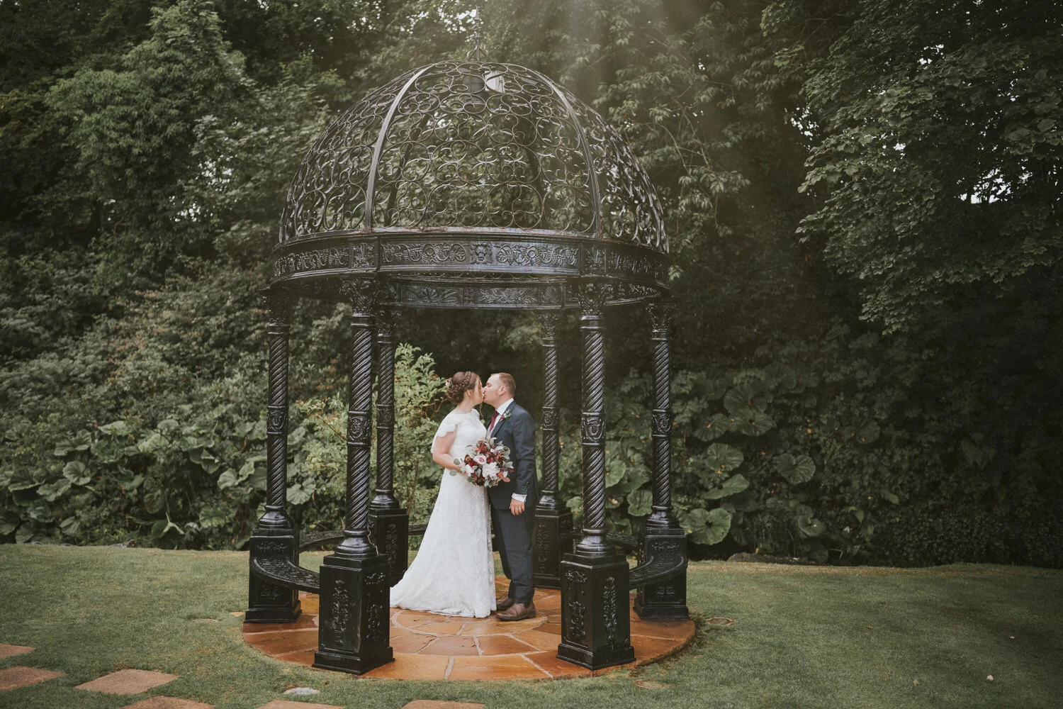 Bride and groom kissing inside an ornate iron gazebo in the gardens at their Ballygally Castle wedding