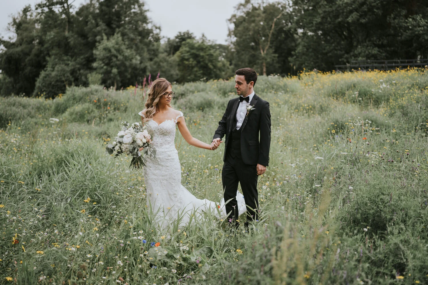 Bride and groom holding hands in a meadow of wildflowers at Roe Valley Resort