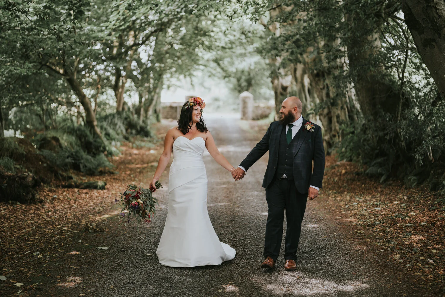 Bride and groom holding hands on a tree lined gravel drive at Breckenhill, County Antrim