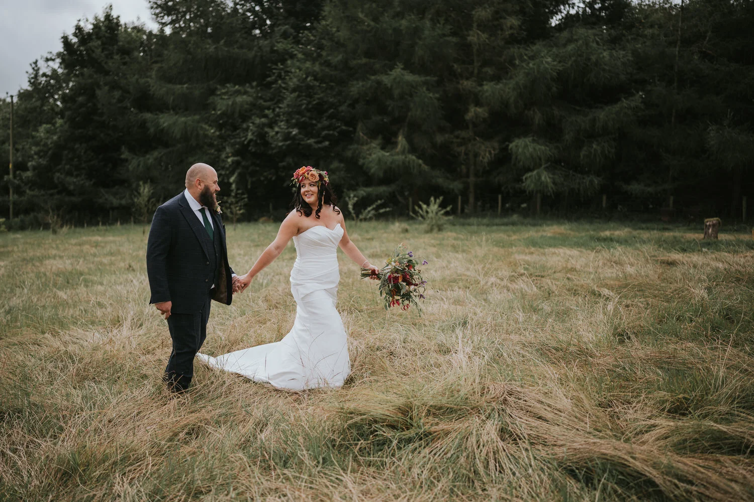 Bride and groom walking hand in hand through long grass in a field at Breckenhill
