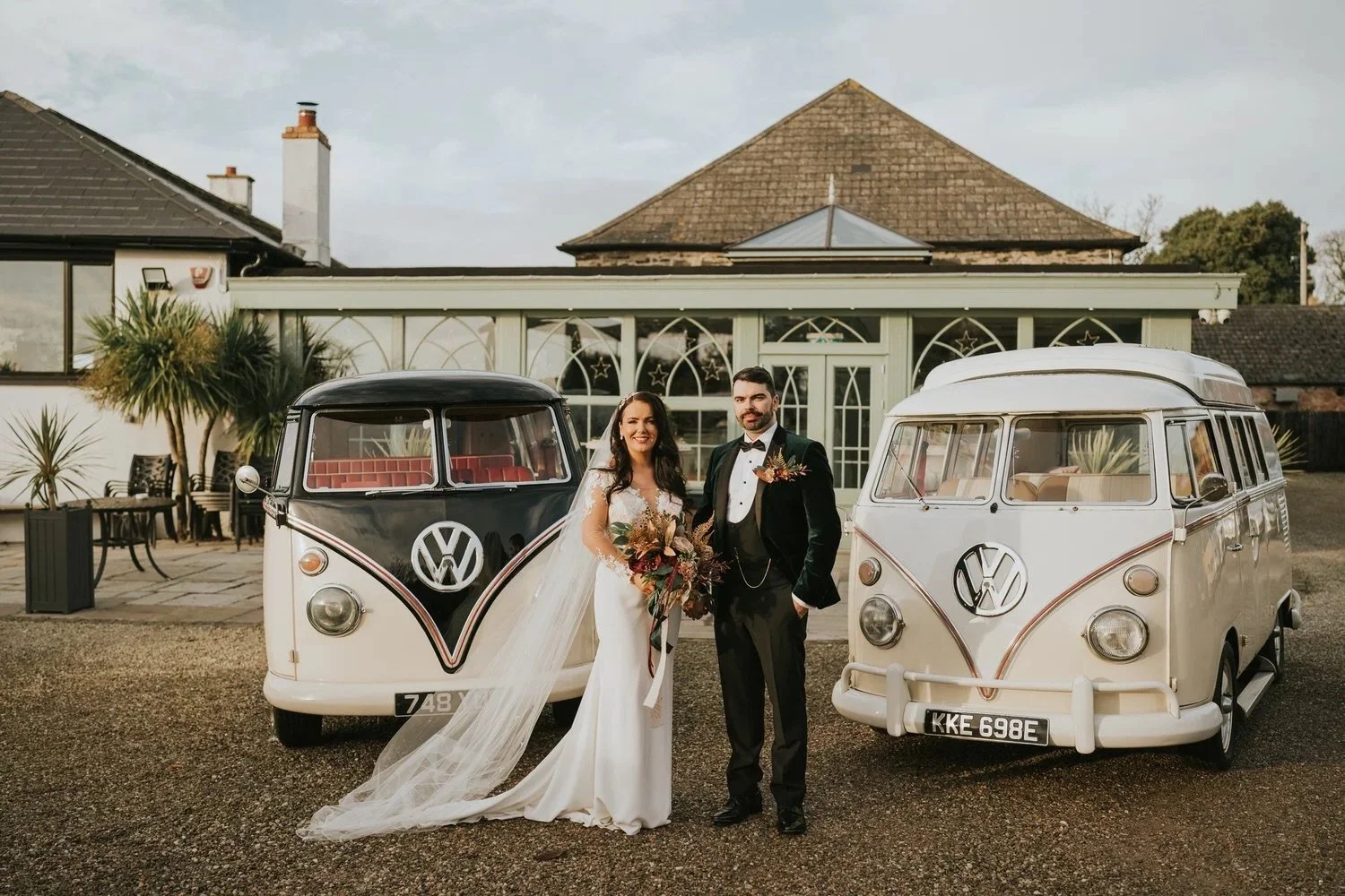 Bride and groom standing together between two vintage VW campervans outside Orange Tree House wedding venue in Greyabbey County Down photographed by Pure Photo N.i