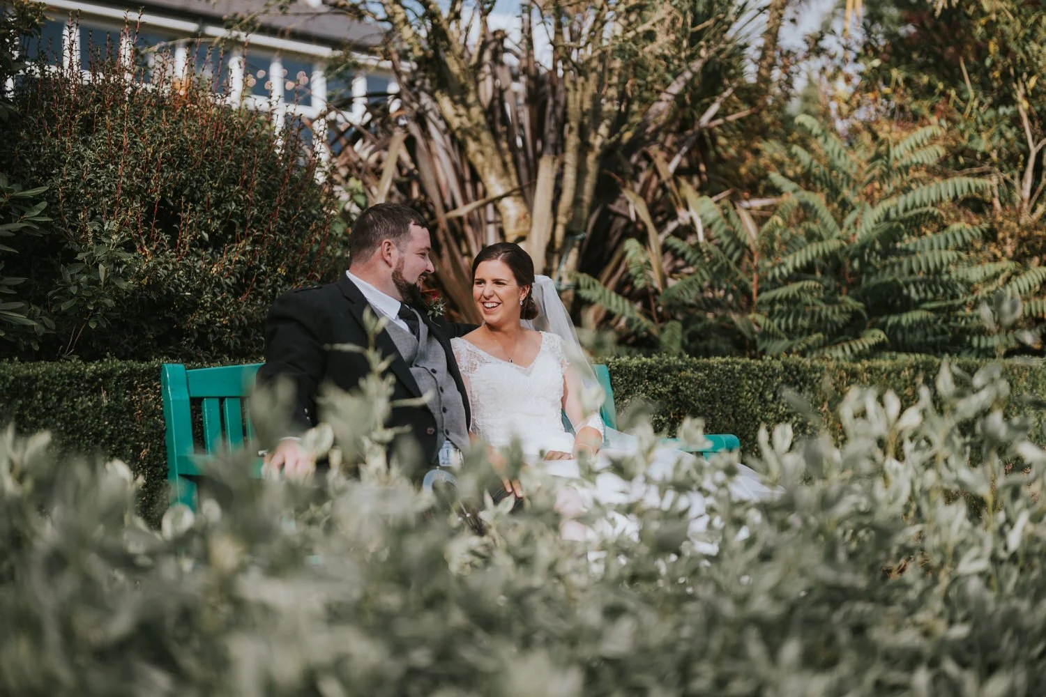 Bride and groom laughing together on a green garden bench at Corick House