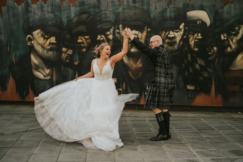 Groom twirling his bride in front of a street art mural on their Titanic Hotel Belfast wedding day