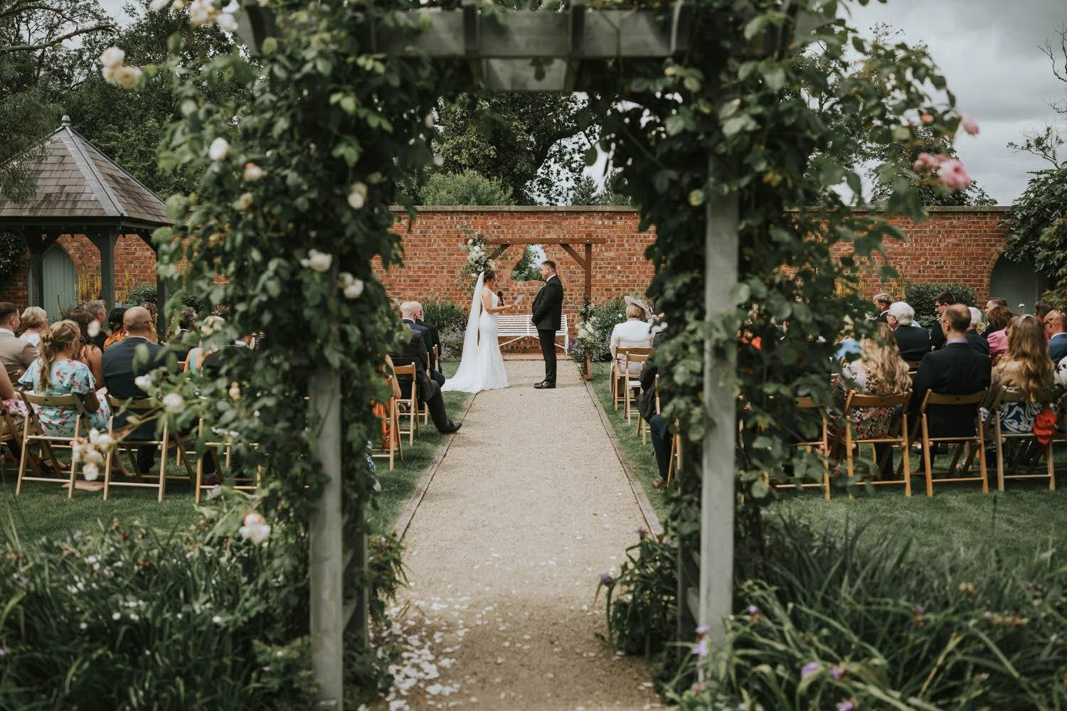 Wedding ceremony in the walled garden at Tullyveery House, seen through a rose covered pergola with the couple at the end of the aisle