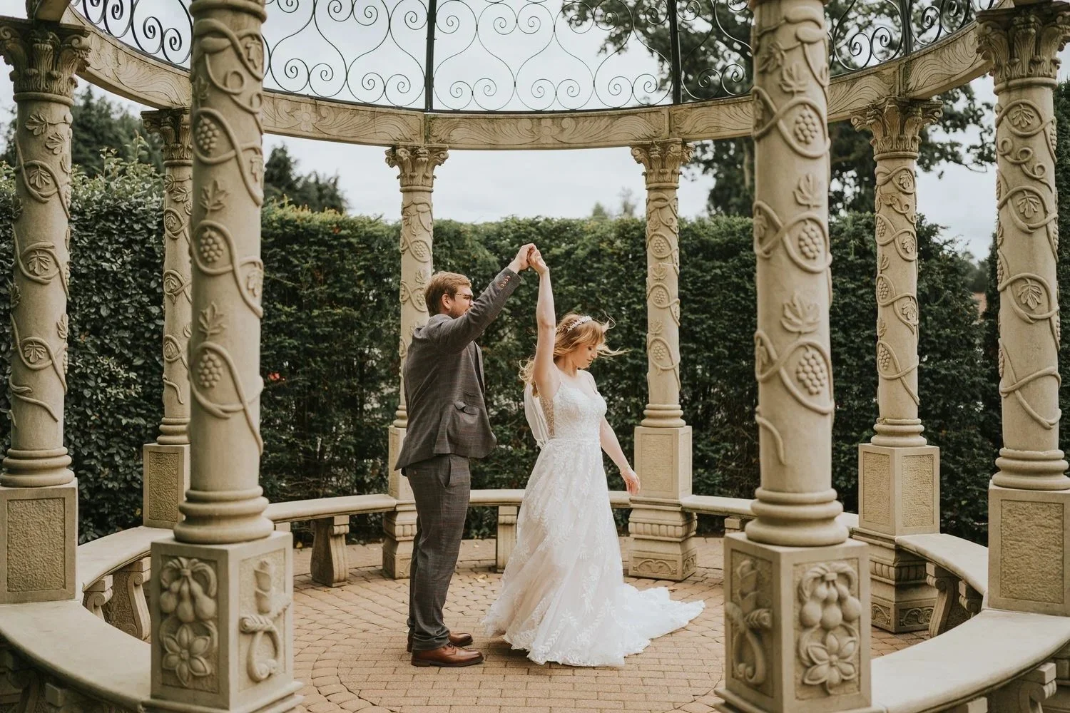 A groom spinning his bride inside the ornate stone gazebo in the grounds of Tullyglass Hotel Ballymena photographed by Pure Photo NI