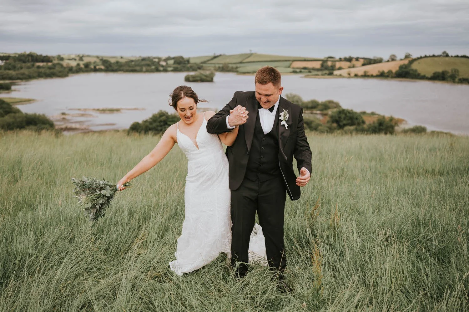 Bride and groom walking through a grassy field with the water behind them at Tullyveery House