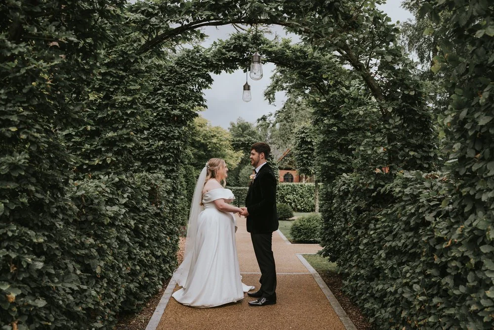 Bride and groom holding hands beneath a clipped hedge archway in the gardens at Clandeboye Lodge, Bangor