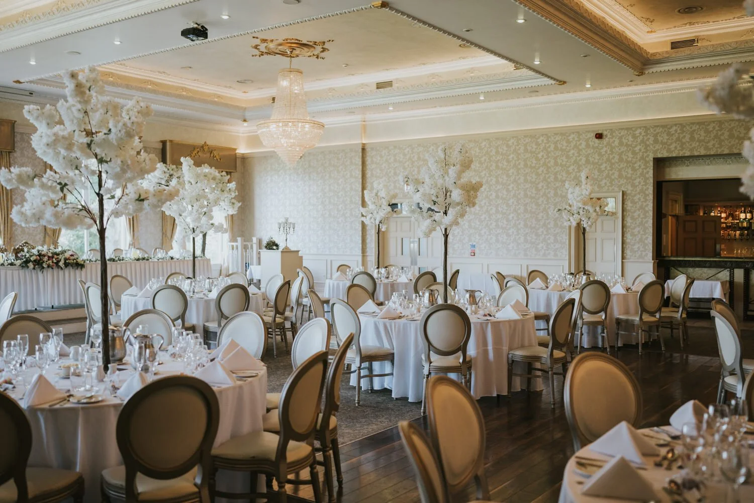 Ballroom set for a wedding with round tables and white blossom trees at Corick House Hotel and Spa