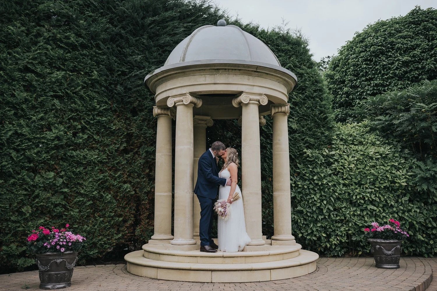 A bride and groom sharing a kiss under the stone rotunda in the grounds of Tullyglass Hotel Ballymena photographed by Pure Photo NI