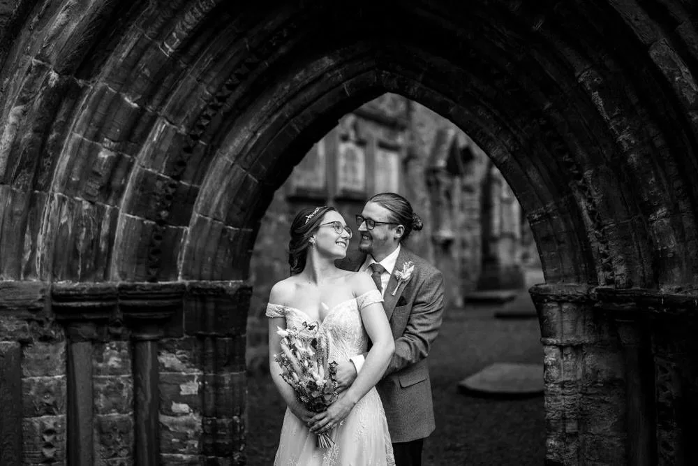 Bride and groom smiling together framed by a stone archway at Greyabbey ruins near Orange Tree House wedding venue photographed by Pure Photo NI