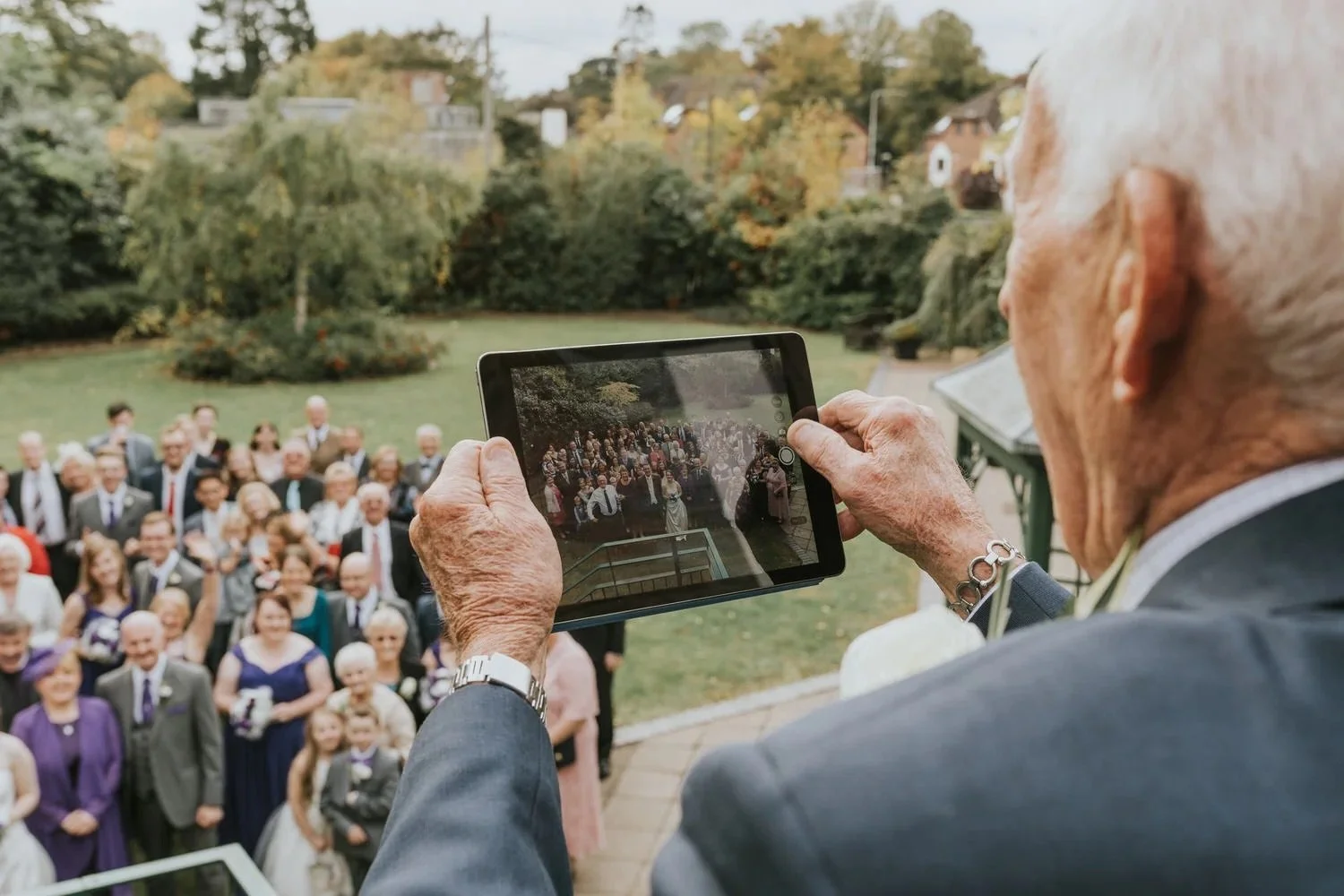 Wedding guest photographing the group formal photo on a tablet from the balcony above