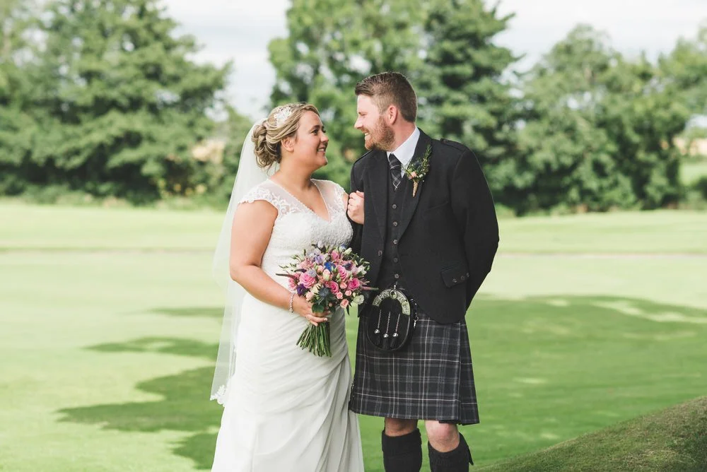 Bride and groom in a kilt laughing together on the lawn beside the golf course at Edenmore House