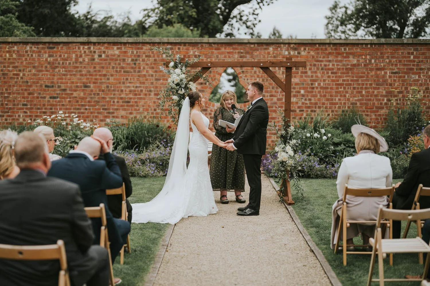 Bride and groom exchanging vows in the walled garden at Tullyveery House, with guests seated on wooden chairs