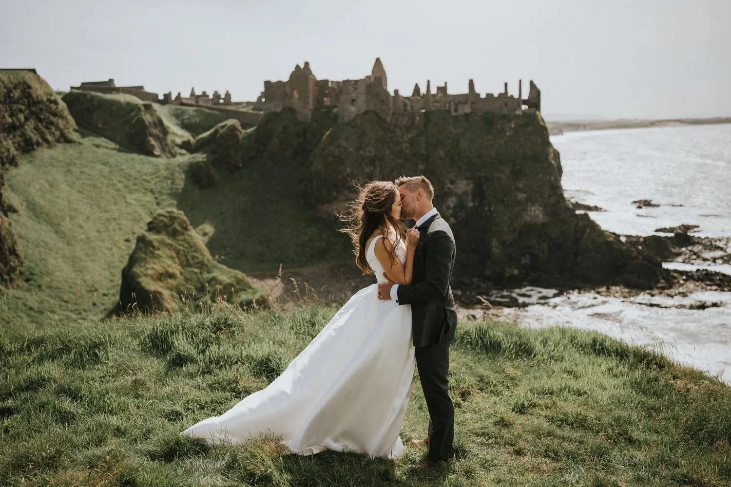 Bride and groom sharing a kiss on the clifftop at Dunluce Castle during their elopement on the Causeway Coast in Northern Ireland, photographed by Pure Photo NI