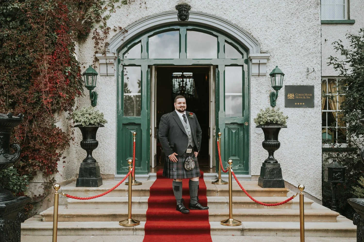 Groom standing on the red carpet at the entrance of Corick House Hotel and Spa