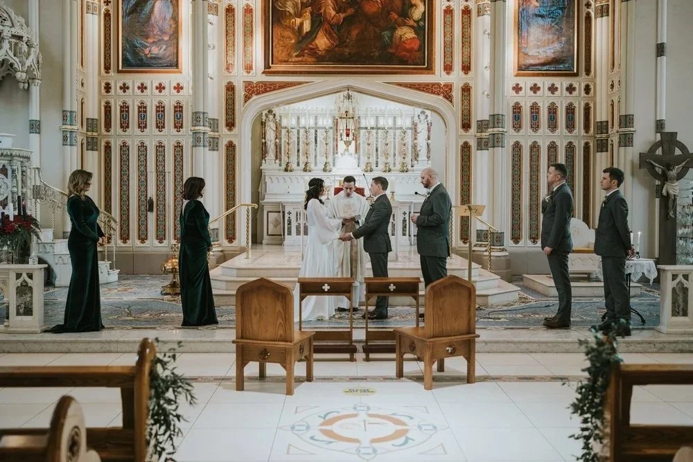 Bride and groom exchanging vows at the altar of a grand church, surrounded by their wedding party, photographed by Pure Photo N.I