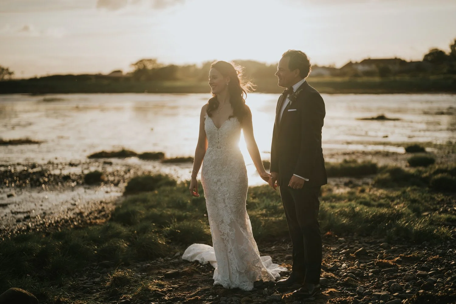 Bride and groom holding hands on the shore of Strangford Lough at sunset at Orange Tree House, Greyabbey