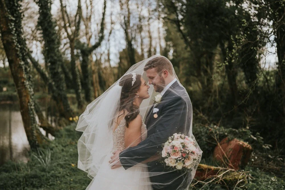 Zara and Jamie touching noses beneath the bride's veil in the woodland at Leighinmohr
