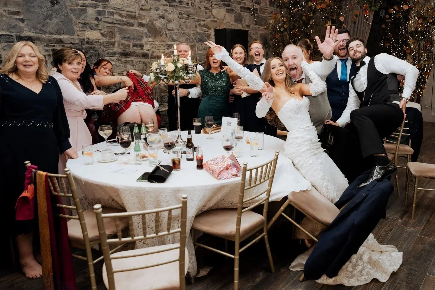 Bride surrounded by family and friends at a table, everyone laughing and celebrating together with genuine, uninhibited joy