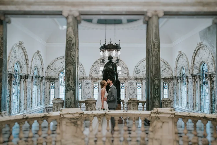 Bride and groom kissing beneath the marble columns inside Belfast City Hall
