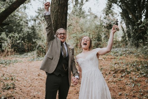 Claire and Chris laughing and cheering with raised arms among the trees at Orange Tree House