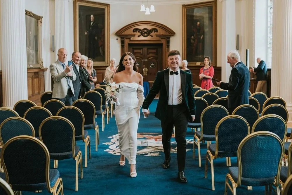 Bride and groom walking back down the aisle after their micro wedding ceremony at Belfast City Hall, surrounded by a small group of close family and friends, photographed by Pure Photo NI