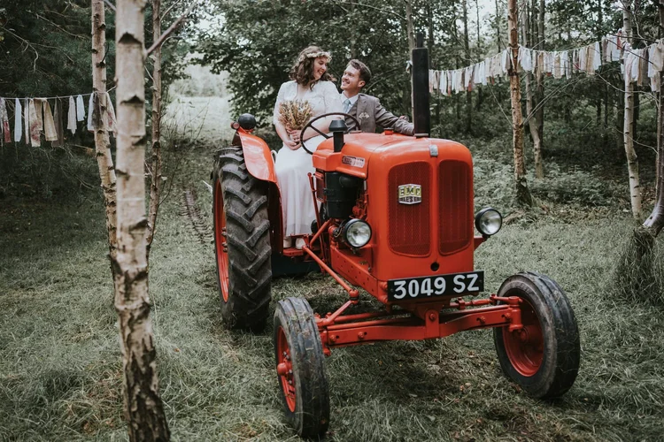 Bride and groom sitting on a vintage red tractor at their woodland wedding in Carraig Woods, Banbridge