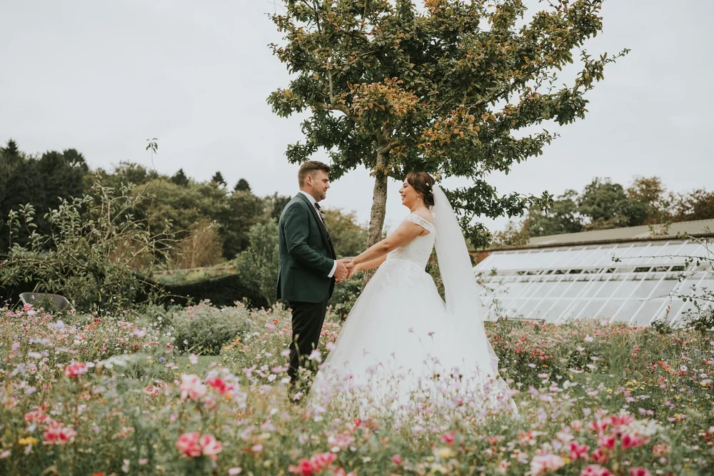 Eilisea and Josh holding hands among wildflowers on their Clandeboye Lodge wedding day