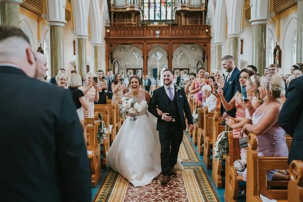 Bride walking down the aisle with her father to a joyful, cheering crowd at a church wedding, photographed by Pure Photo N.I