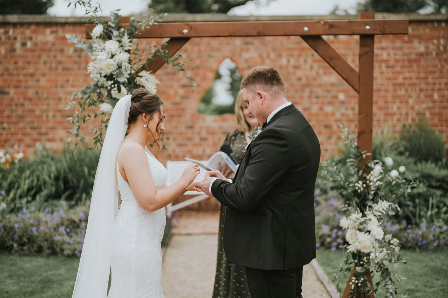 Bride and groom holding hands at the red brick wall in the walled garden at Tullyveery House