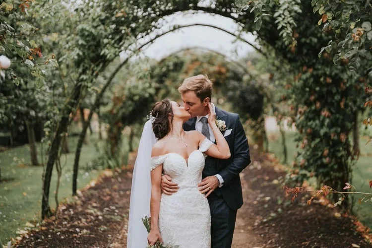 Bride and groom beneath a leafy garden archway in the grounds of Bangor Castle
