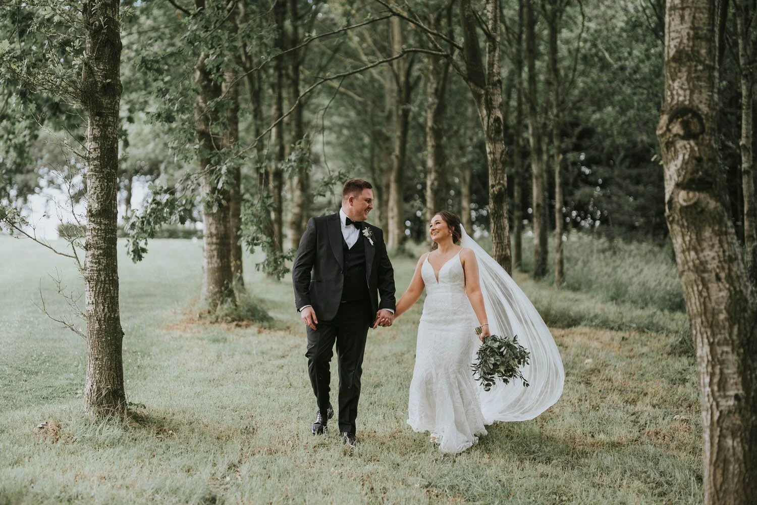 Emily and Tom's wedding at Tullyveery House, the couple walking through a tree lined grassy area