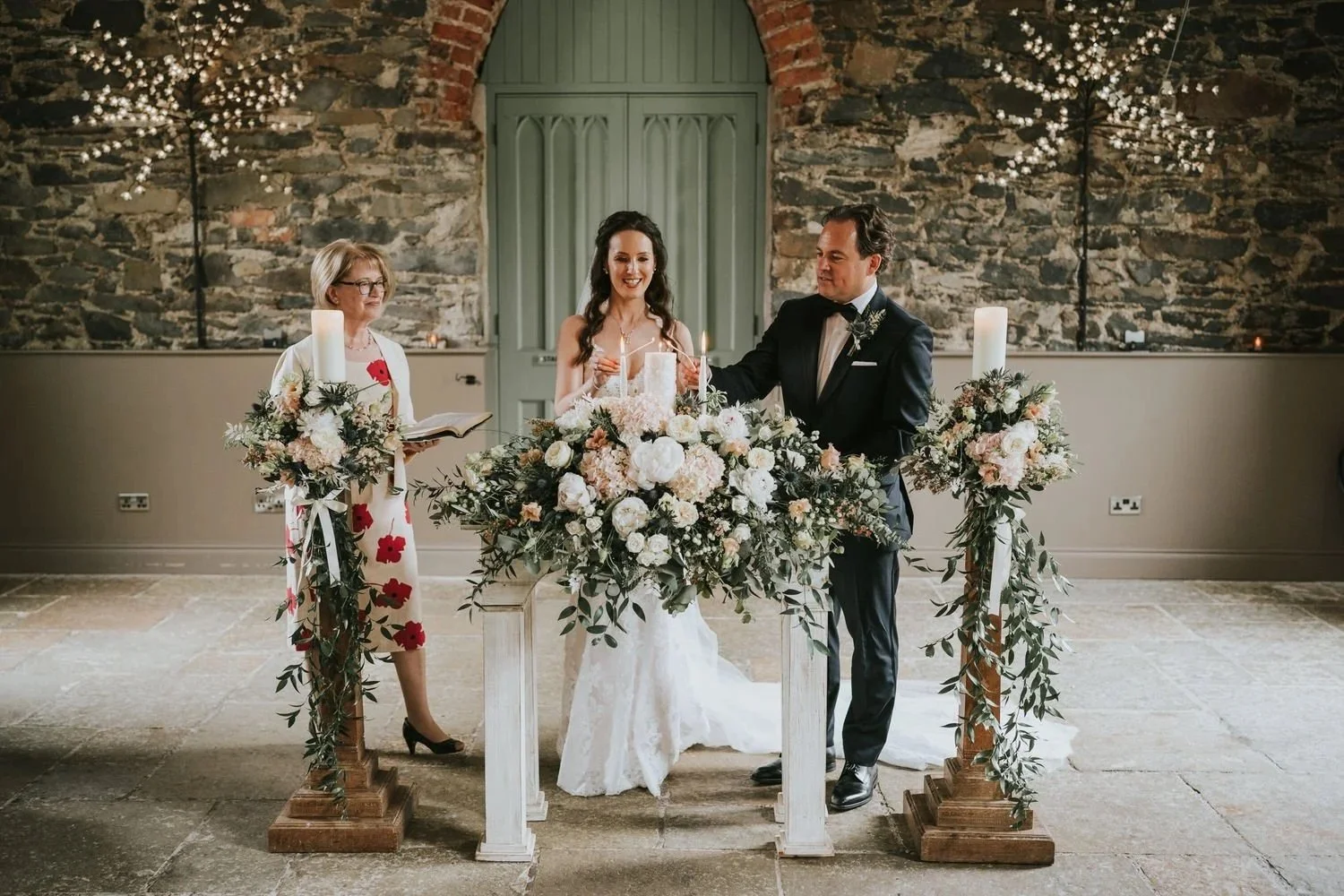 Bride and groom lighting a unity candle during their wedding ceremony in the stone walled function room at Orange Tree House