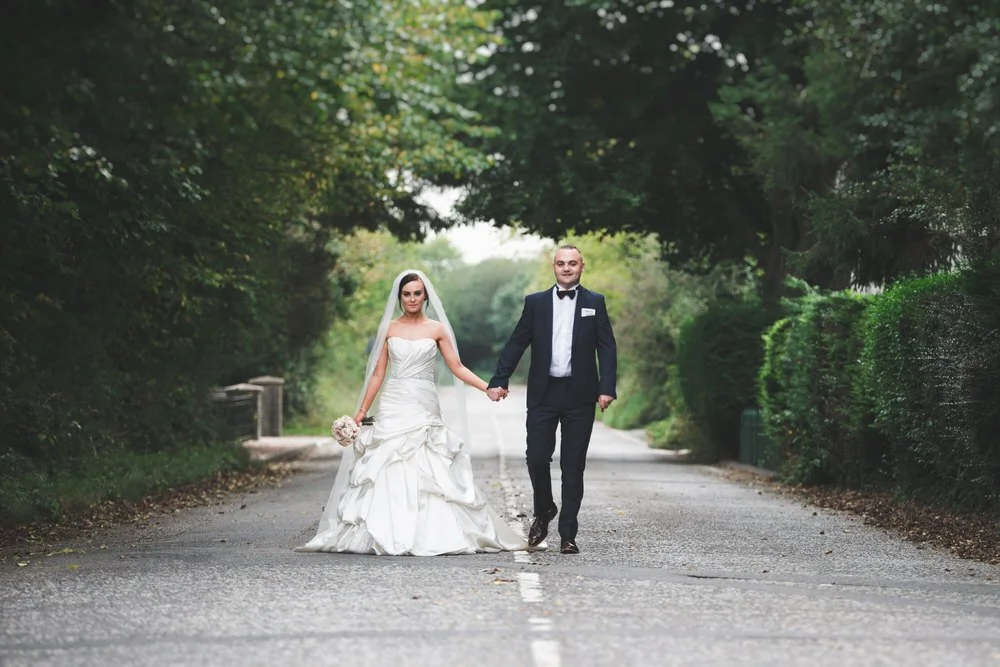 Bride and groom holding hands and walking down a tree lined country road at their Dunsilly Hotel wedding near Antrim