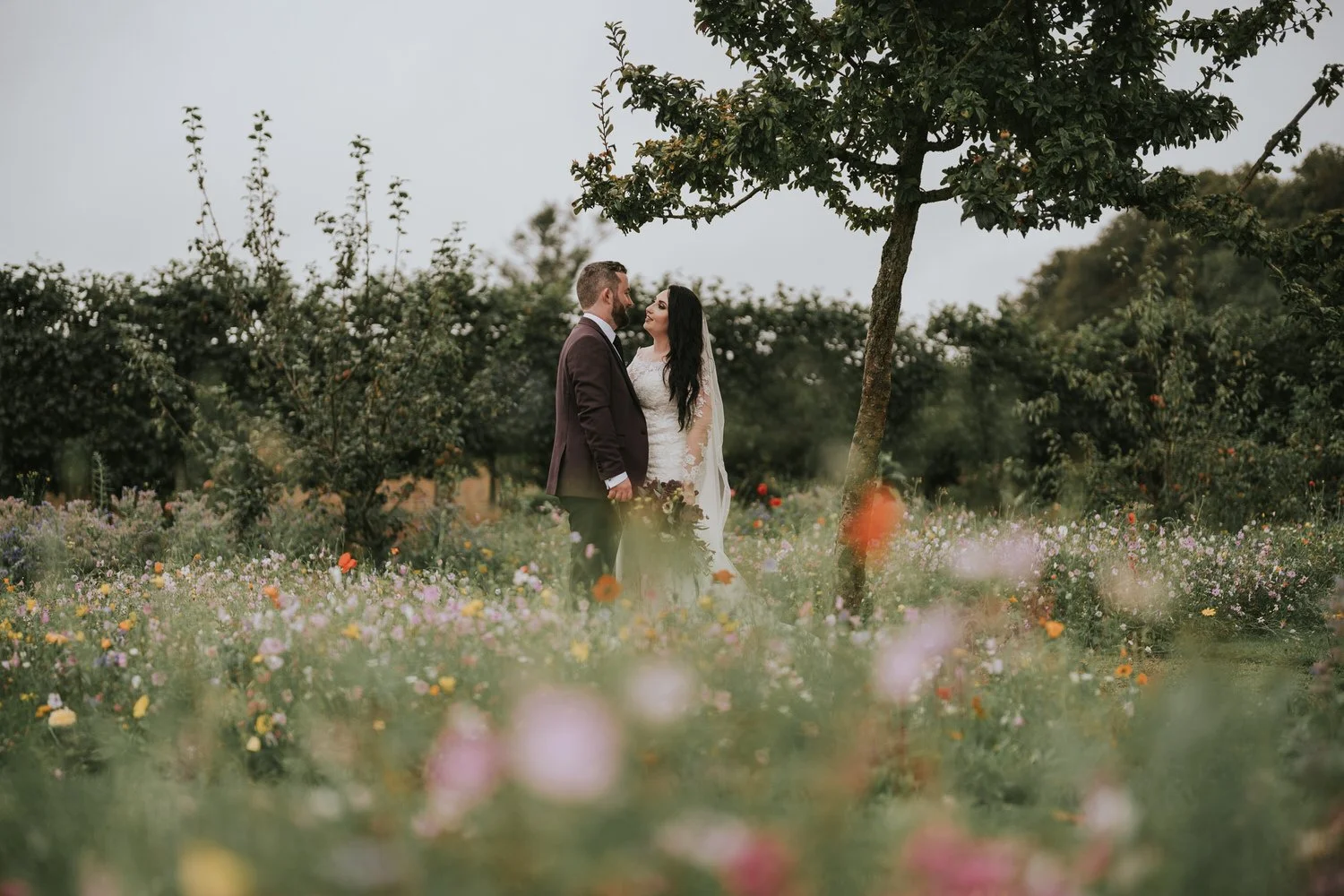 Bride and groom embracing among wildflowers with trees behind them at Bangor Castle