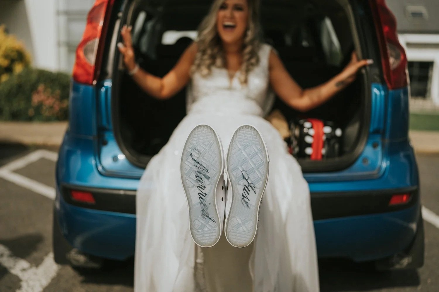Bride's feet in comfortable white trainers with "I said yes" written on the soles, bridesmaids laughing joyfully in the background