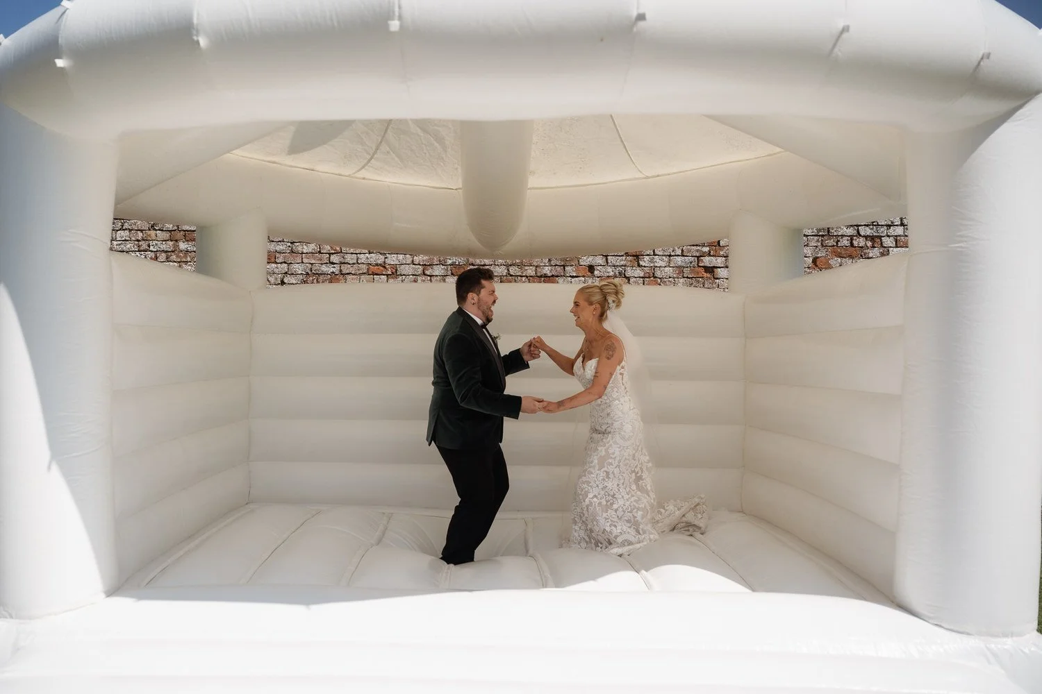 Bride and groom playfully dancing together inside a bouncy castle in their wedding attire, embracing an unexpected moment of joy