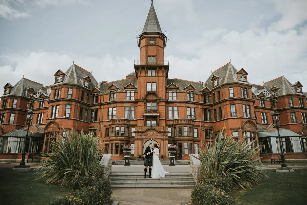 Bride and groom standing on the steps in front of the red brick Slieve Donard hotel in Newcastle, County Down