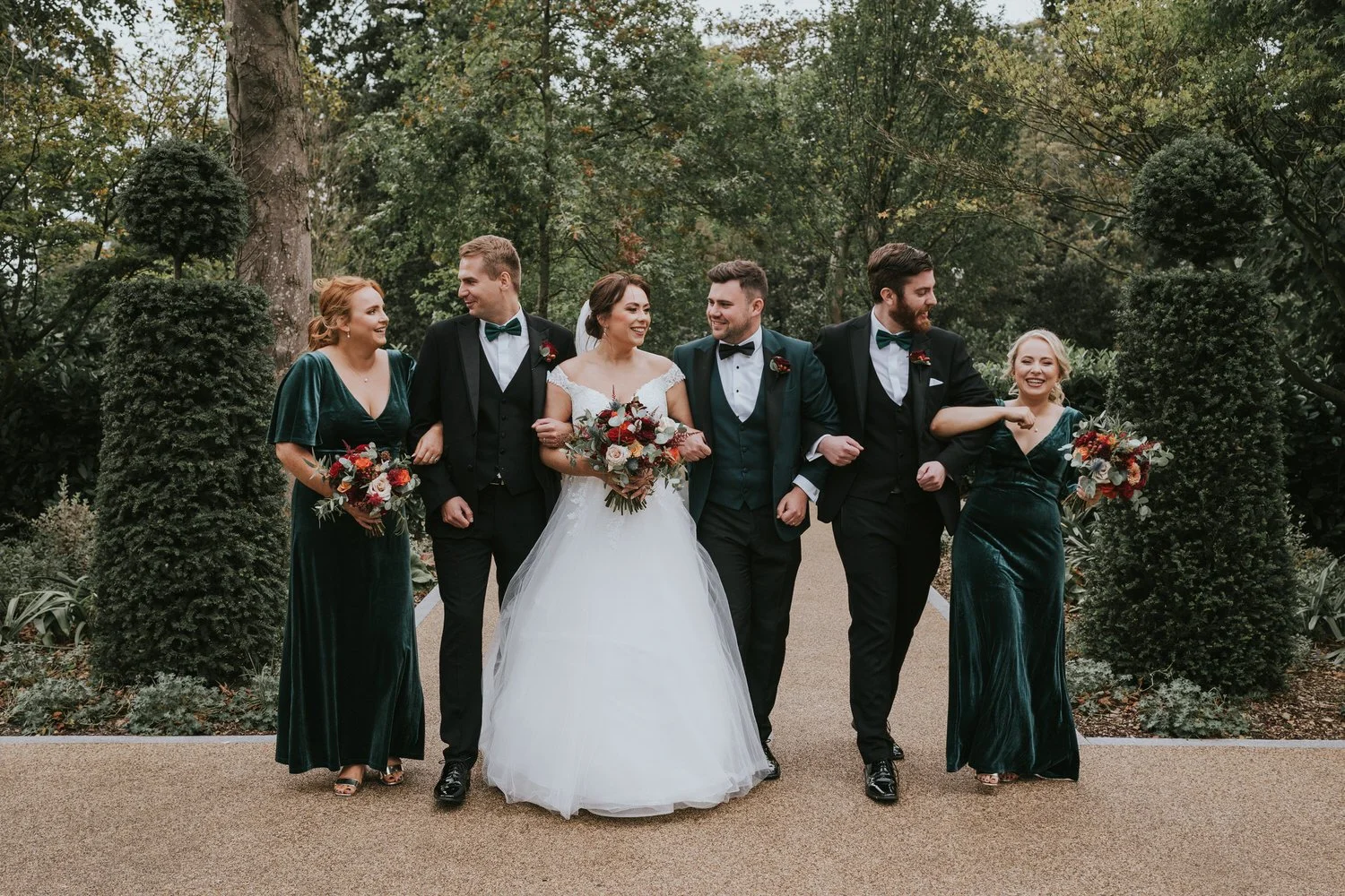 Bride and groom walking along a gravel path with their wedding party in the gardens at Clandeboye Lodge