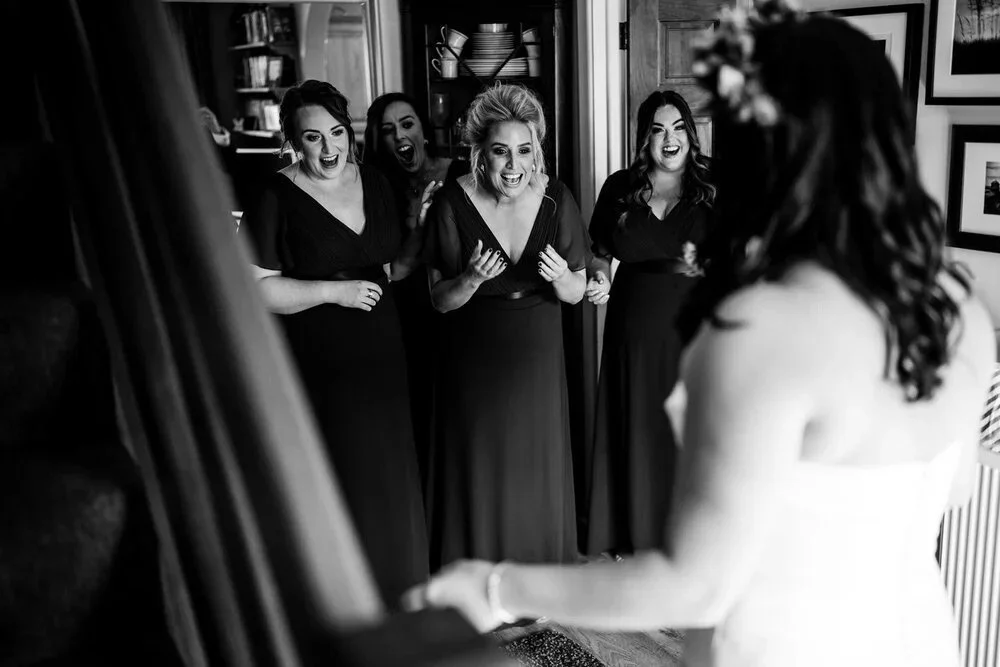 Bridesmaids reacting with joy and tears as they see the bride in her wedding dress for the first time, black and white photograph by Pure Photo N.I